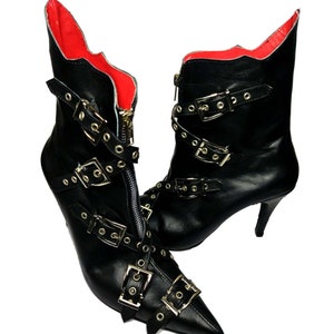 Puede incluir: Un par de botines de cuero negro con punta y tacones de aguja. Los botines presentan m&uacute;ltiples hebillas plateadas y cierre de cremallera. El forro interior es rojo.