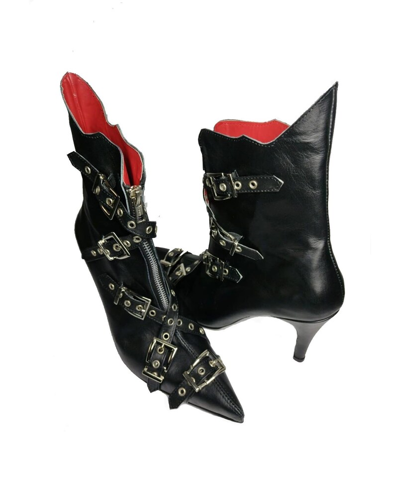 Puede incluir: Botines de cuero negro con punta y tacones de aguja. Las botas tienen m&uacute;ltiples hebillas plateadas y cierre de cremallera. El forro interior es rojo.
