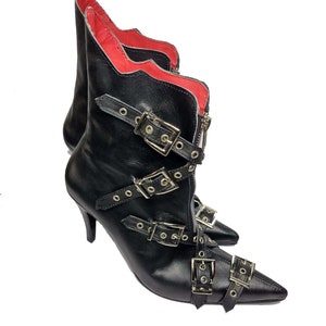 Puede incluir: Botines de cuero negro con puntera y m&uacute;ltiples hebillas plateadas. Las botas tienen cierre de cremallera y forro interior rojo. Los tacones son de estilo stiletto.