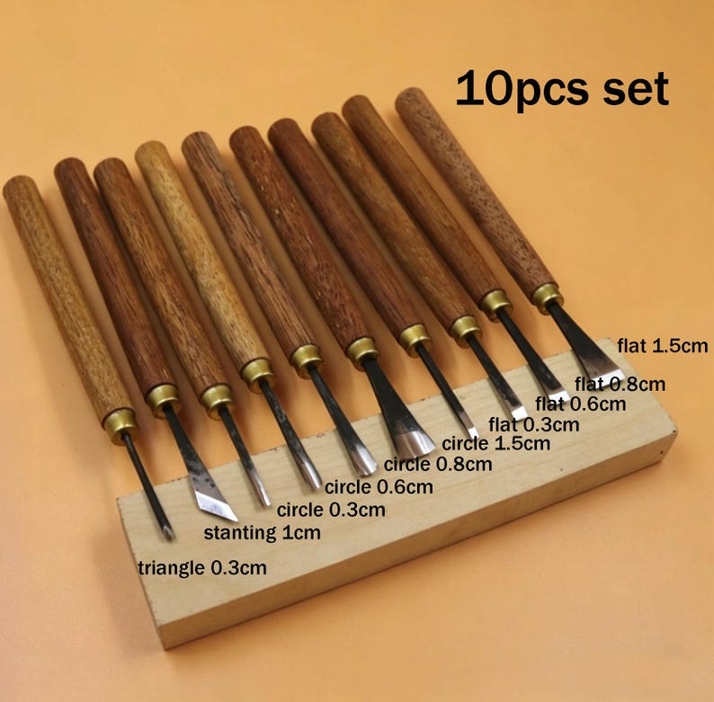 Op de afbeelding: Een set van tien houtsnijgereedschappen met houten handvatten en metalen messen. De messen hebben verschillende vormen, waaronder plat, cirkel, driehoek en schuin, met maten vari&euml;rend van 0,3 cm tot 1,5 cm. De tekst "10pcs set" is zichtbaar.