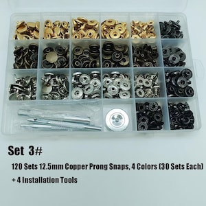 May include: A clear plastic storage container filled with 120 sets of 12.5mm copper prong snaps in four colors, including gold, bronze, silver, and black. The kit includes four metal installation tools and a circular setting base.
