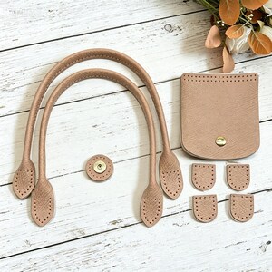 Peut inclure: Un ensemble de composants de sac beiges texturés comprenant deux anses arquées, une poche carrée avec un bouton-pression doré, une attache ronde et quatre petites languettes semi-circulaires, toutes avec des trous pré-perforés pour la couture.