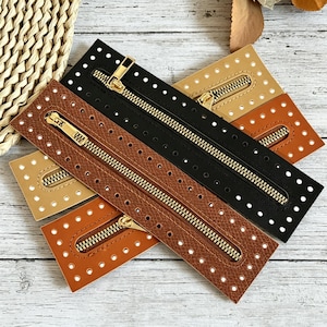 May include: A collection of rectangular leather zipper panels in black, tan, and brown. Each panel features a central gold-tone metal zipper and a border of evenly spaced pre-punched holes along the edges for sewing or attachment purposes.