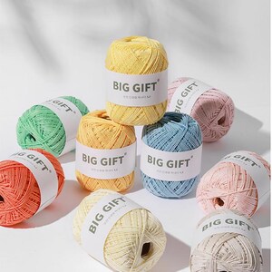 May include: A collection of nine yarn balls in various pastel and vibrant colours, each wrapped in a white paper band labelled BIG GIFT. The yarn is textured and wound into compact, rounded shapes, displayed together in a group.