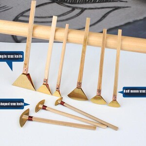 May include: A selection of wax knives with wooden handles and brass blades. The blades are in various shapes, including triangle, fan, and half-moon. The image text reads "Triangle wax knife", "Fan shaped wax knife", and "Half moon wax knife".