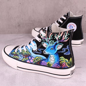 May include: Black high-top canvas sneakers with a hand-painted design featuring a blue deer, green foliage, and a flowing stream. The sneakers have white soles and black laces. The brand name "DABOWEN" is printed on the side of the shoe.