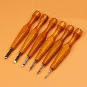 May include: Six wood carving tools with polished wooden handles and silver blades are arranged diagonally on an orange background. The tools are designed for detailed woodworking and carving projects.