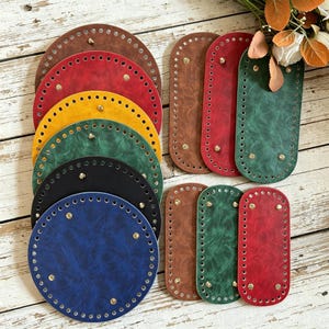 May include: A collection of circular and oval-shaped faux leather bag bases in brown, red, yellow, green, black, and blue. Each piece features pre-punched holes along the perimeter for stitching and small gold-toned metal feet attached to the surface.