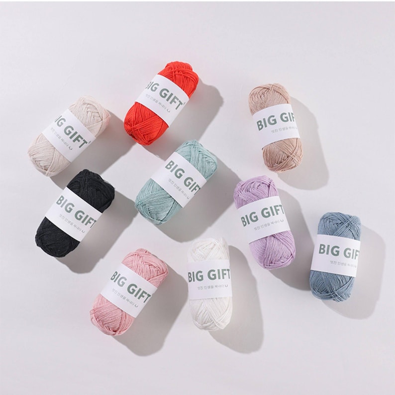 May include: Nine small skeins of yarn in various colors including red, black, white, pink, light blue, lavender, beige, and sage green. Each skein is wrapped with a white paper band featuring the text BIG GIFT printed in dark gray lettering.