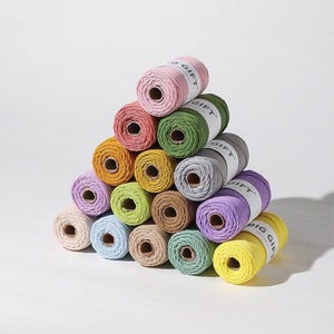 May include: A pyramid stack of fifteen spools of cotton cord in various colors including pink, green, yellow, blue, purple, gray, and brown. Each spool features a white paper label with the text BIG GIFT printed in black.