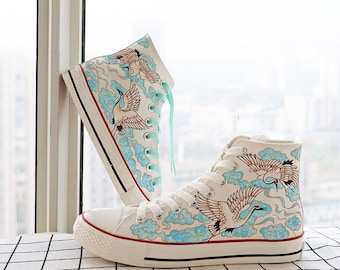 Op de afbeelding: Witte hoge canvas sneakers met een blauw en wit kraanvogel- en wolkendesign.
