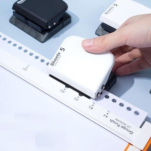 May include: A white and black paper punch tool with the text Sheets 5 Gauge Punch printed on the top. The device is positioned on a white paper guide labeled with A4, B5, A5, and All, featuring the text Gauge Punch and model number LD-302620N.