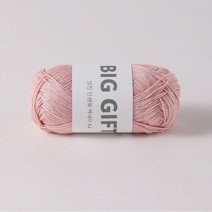 May include: A cylindrical skein of soft pastel pink yarn wrapped in a white paper band. The band features the bold text BIG GIFT in dark gray capital letters, accompanied by smaller Korean text and a small heart icon printed on the side.