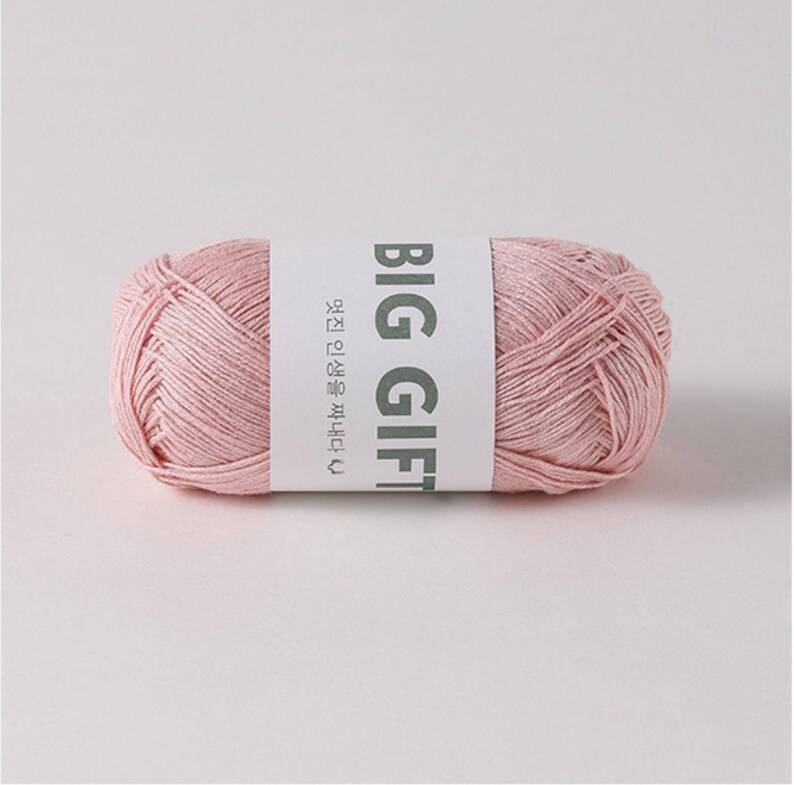May include: A cylindrical skein of soft pastel pink yarn wrapped in a white paper band. The band features the bold text BIG GIFT in dark gray capital letters, accompanied by smaller Korean text and a small heart icon printed on the side.