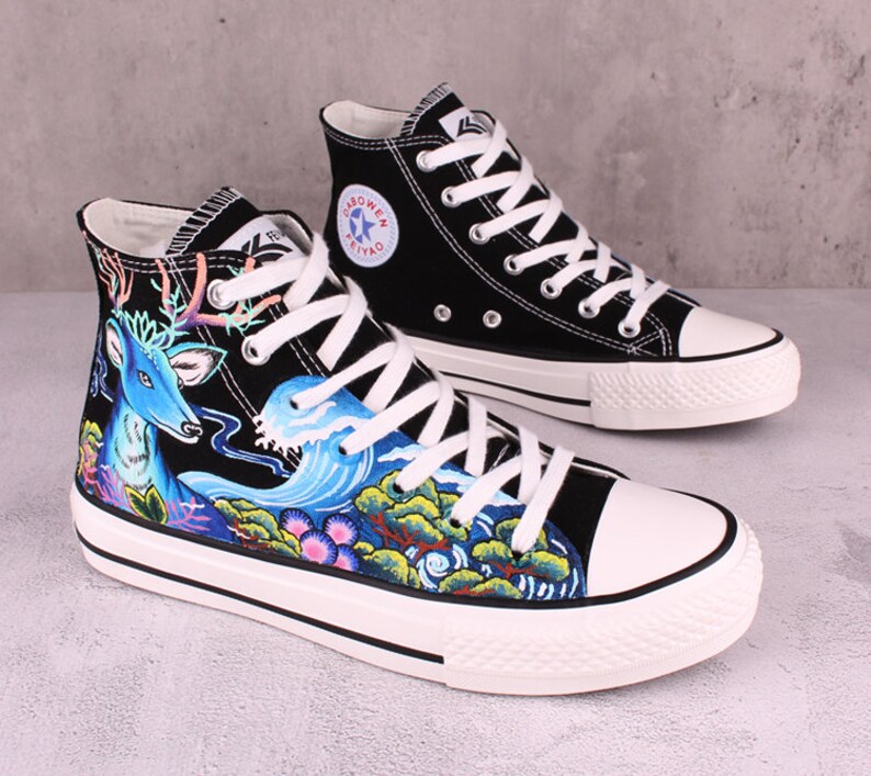 May include: Black high-top canvas sneakers with a blue deer and wave design. The sneakers have white laces and a white sole.