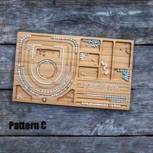 May include: A wooden jewelry organizer with multiple compartments and grooves, filled with necklaces, bracelets, and loose beads. The text "Pattern C" is displayed in the lower left corner. The jewelry includes pearls and light blue beads.