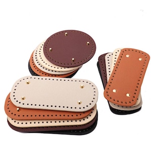 May include: A collection of leather bag bases in various colors, including black, brown, tan, and orange. The bases are oval and rectangular, with pre-punched holes for stitching and gold-colored rivets.