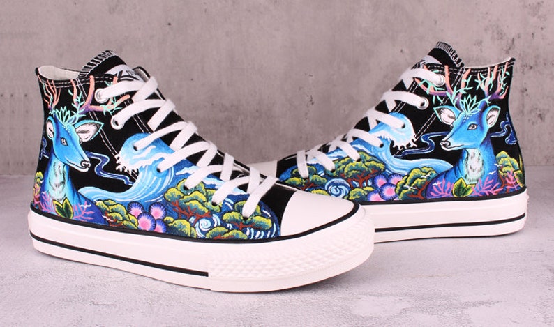 May include: A pair of black high-top canvas shoes with a colorful hand-painted design featuring a blue deer, waves, and trees.