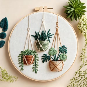 May include: Embroidered hoop art featuring three hanging planters with detailed green plants. The planters are in woven baskets and macrame hangers. The background is a neutral canvas, with additional embroidered leaves.