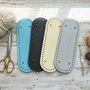 May include: Four oval-shaped bag bases in light blue, black, cream, and silver, each featuring pre-punched holes along the perimeter and four small gold-toned metal feet. Each base is embossed with the word Handmade and a small logo.