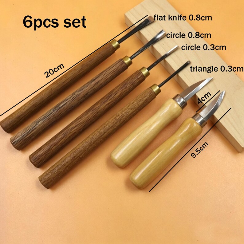 Op de afbeelding: Een 6-delige set houtsnijgereedschap. De set bevat diverse gutsen en messen met houten handvatten en metalen bladen. De langste tool is 20 cm lang. De set bevat een plat mes, cirkel- en driehoeksgereedschap.
