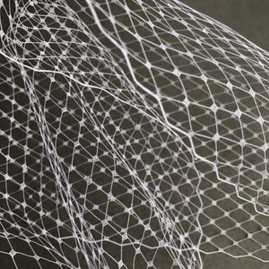 May include: White netting fabric with a diamond pattern. The netting is soft and delicate, and it is perfect for crafting or decorating.