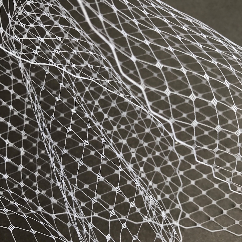 May include: White netting fabric with a diamond pattern. The netting is soft and delicate, and it is perfect for crafting or decorating.