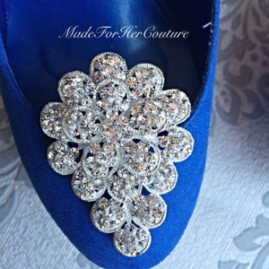 K&ouml;nnte beinhalten: Nahaufnahme eines royalblauen Schuhs mit einem gro&szlig;en, silbernen Strass-Schmuckst&uuml;ck in Form eines Blumenb&uuml;schels. Der Schmuck besteht aus vielen kleinen, klaren Strasssteinen.