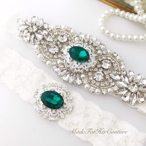 A emerald green accented rhinestone and pearl wedding garter with exquisite detailing for the keepsake garter on a soft lace. The matching toss garter is finished of with the same emerald green gem as the center of the keepsake.