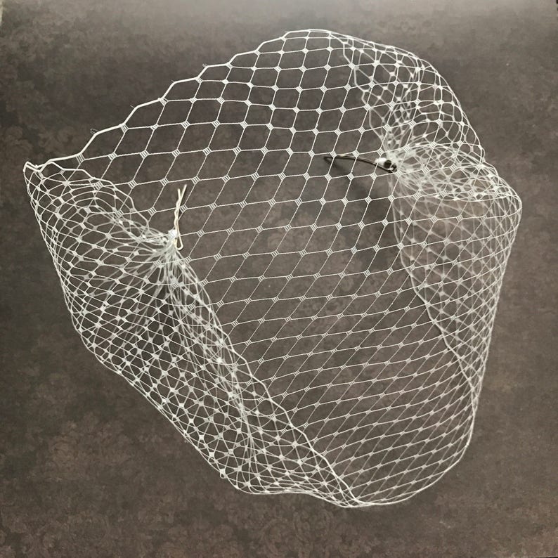 May include: White bridal veil made of delicate netting with a diamond pattern. The veil is gathered at the top and has a simple design.