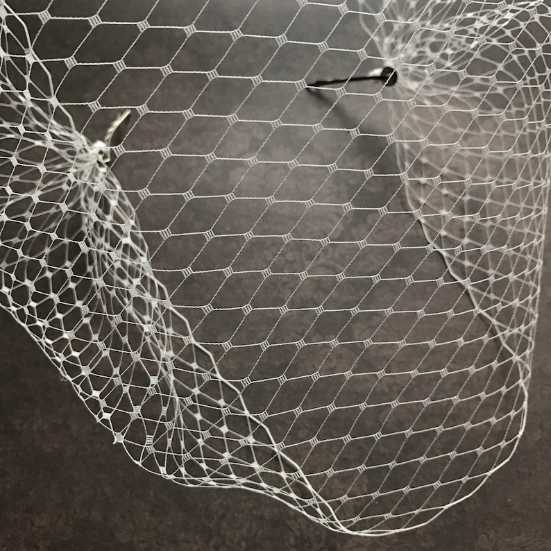 May include: White bridal veil made of fine netting with a diamond pattern. The veil is attached to a comb.