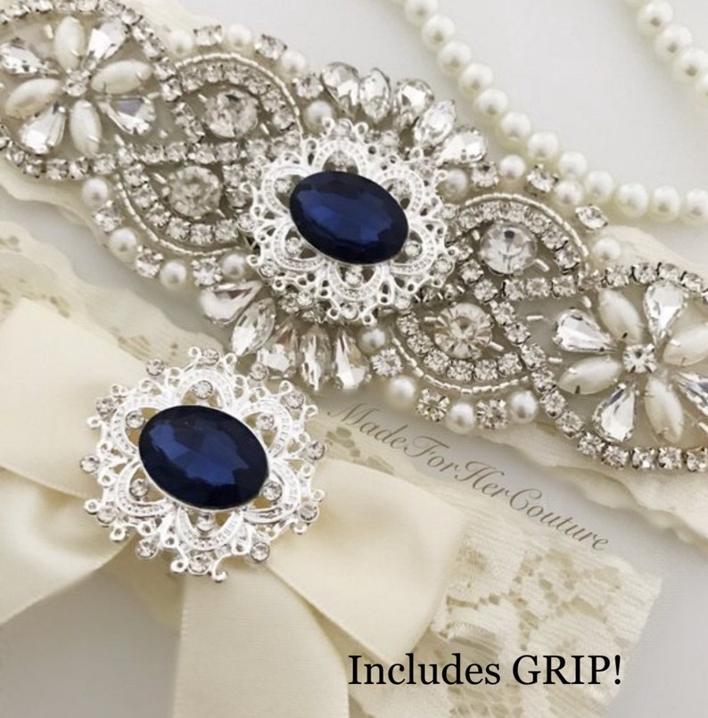 Rhinestone and pearl applique featuring a stunning navy-blue gem in the center on ivory lace for the keepsake garter. Matching toss garter also features the stunning navy-blue gem with a delicate ivory bow. Gem, lace and bow colors can be customized.