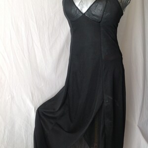 May include: A black slip dress with spaghetti straps and a V-neckline. The dress has a flowing skirt with a high slit, and is displayed on a mannequin. The fabric appears to be a lightweight material.