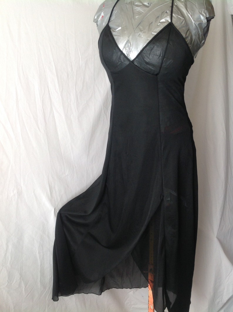 May include: A black slip dress with spaghetti straps and a V-neckline. The dress has a flowing skirt with a high slit, and is displayed on a mannequin. The fabric appears to be a lightweight material.
