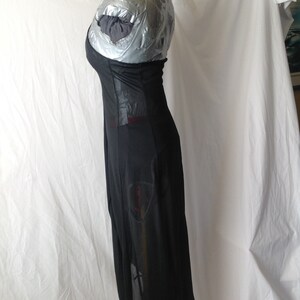 May include: A long, black dress with a sheer skirt and a fitted bodice. The dress has a unique design with cutouts and a flowing silhouette. The dress is displayed on a mannequin covered in silver tape.