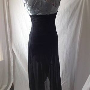 May include: A black, floor-length dress with a halter neckline. The dress is displayed on a mannequin. The skirt has a sheer overlay, revealing the legs. The dress is made of a soft, flowing fabric.