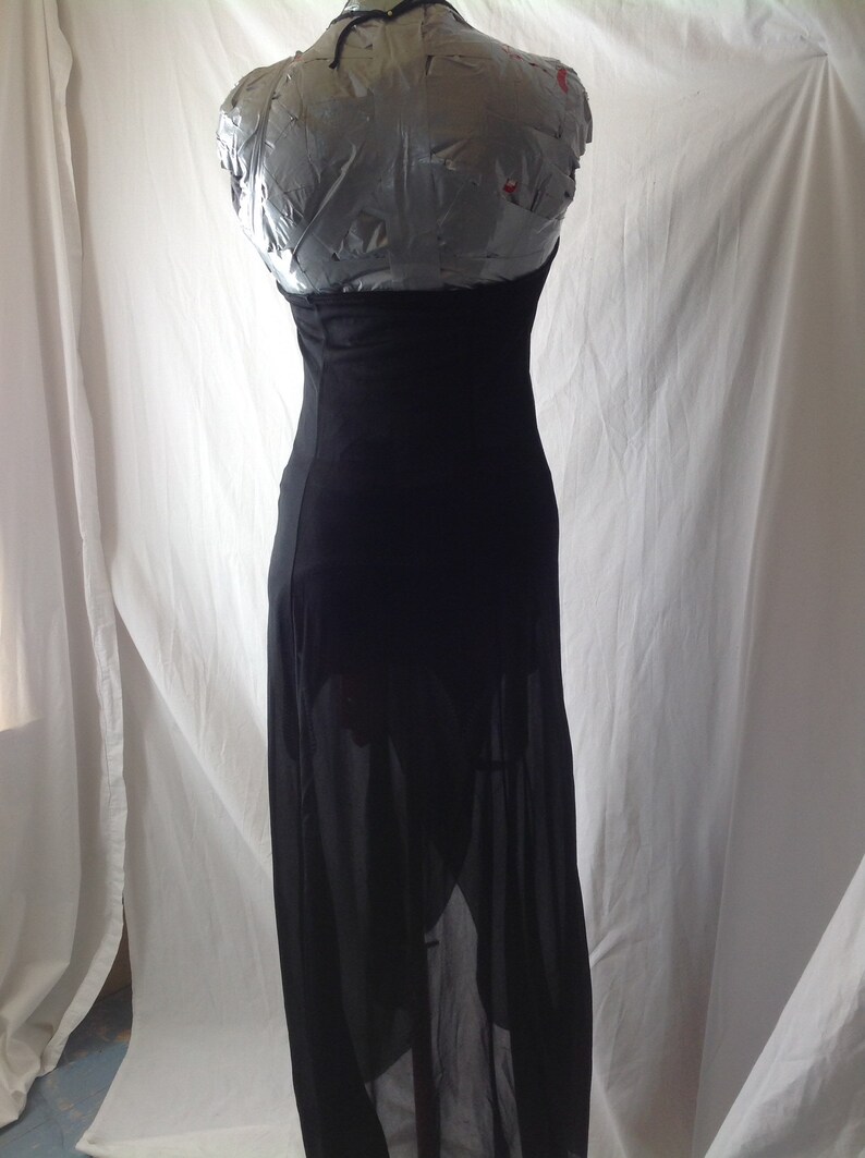 May include: A black, floor-length dress with a halter neckline. The dress is displayed on a mannequin. The skirt has a sheer overlay, revealing the legs. The dress is made of a soft, flowing fabric.