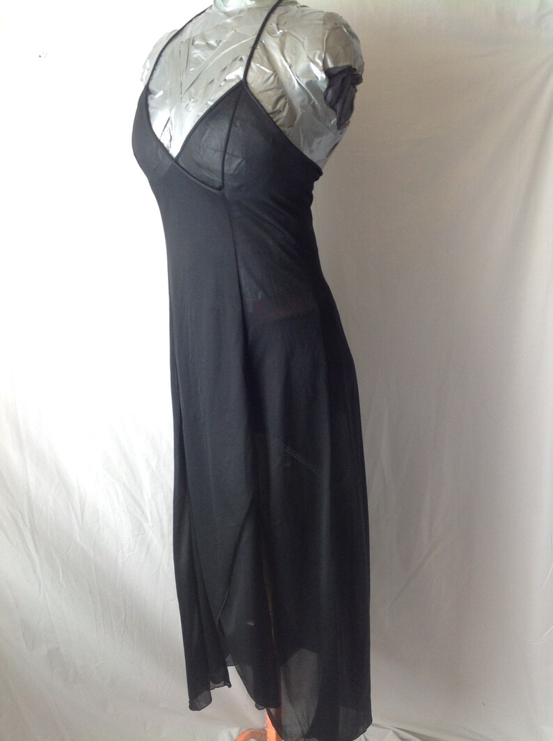 May include: A black halter dress with a V-neckline and a flowing, asymmetrical skirt. The dress is made of a sheer fabric, and the bodice has a solid panel. The dress is displayed on a mannequin.