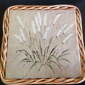 May include: A woven wicker coaster with a square tile featuring a white wheat design on a beige background.