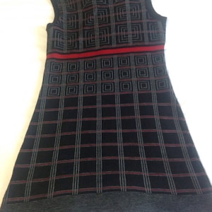 May include: Sleeveless black dress with a geometric pattern. The dress features a high neckline and a red horizontal stripe across the midsection. The pattern consists of squares and lines in gray and red.