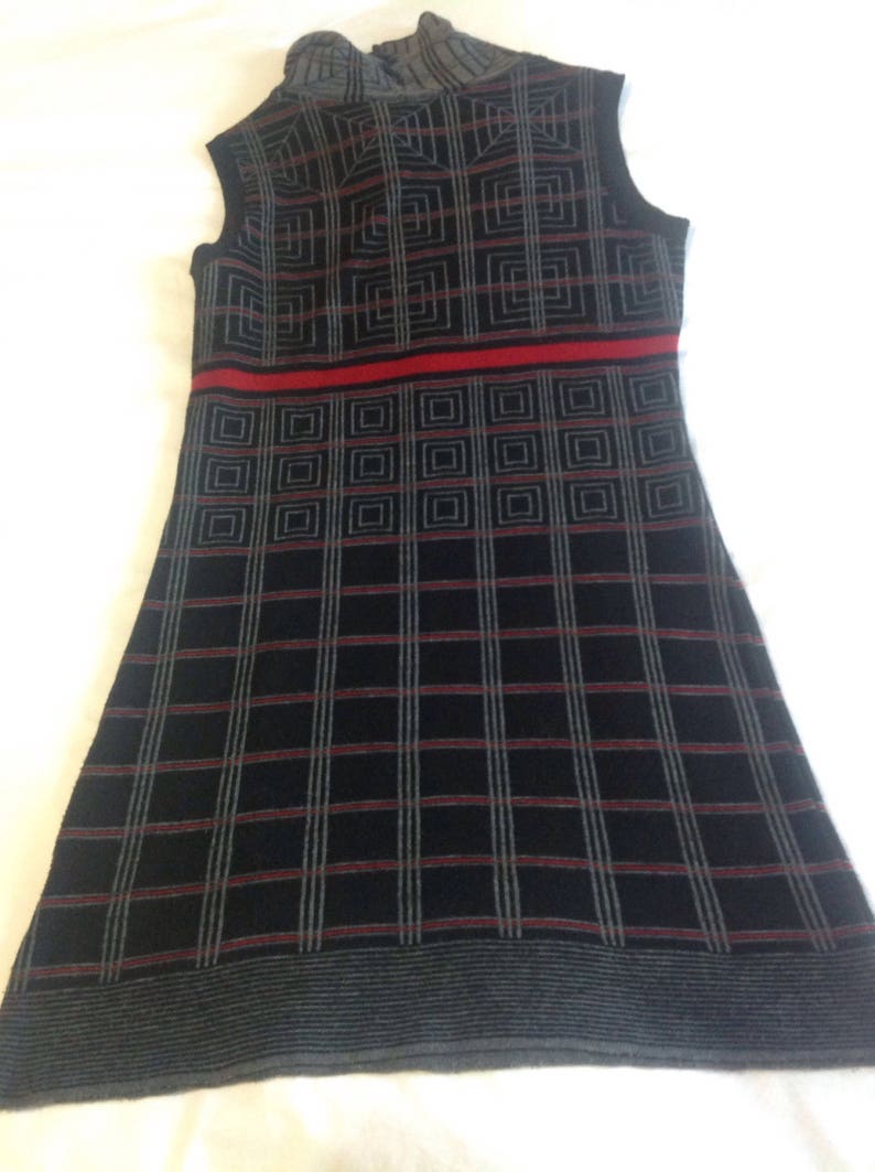 May include: Sleeveless black dress with a geometric pattern. The dress features a high neckline and a red horizontal stripe across the midsection. The pattern consists of squares and lines in gray and red.