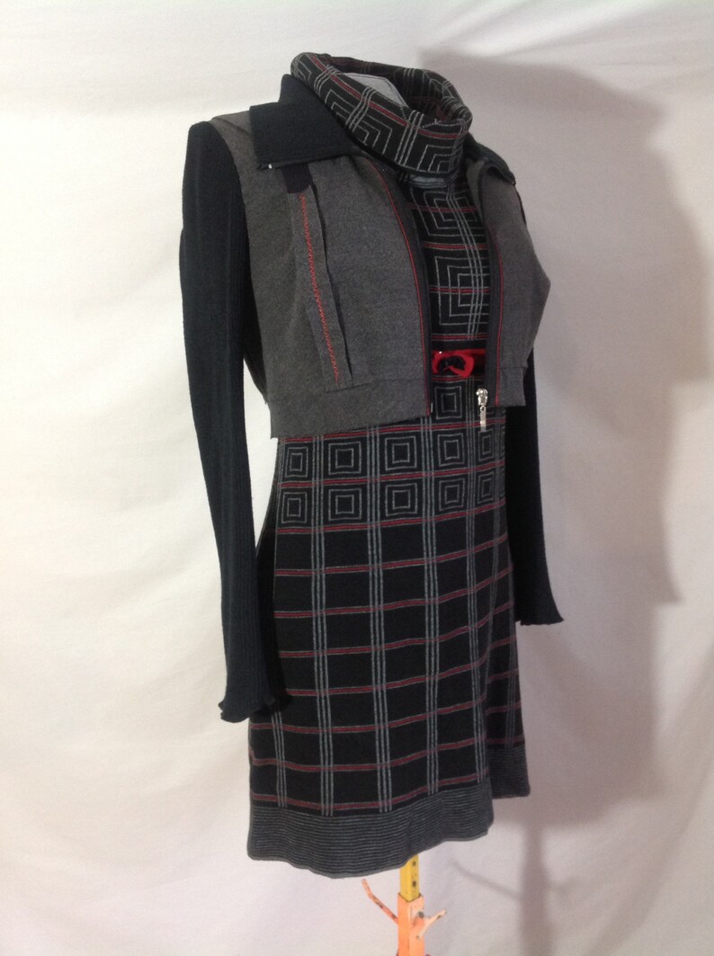 May include: A gray and black dress with a plaid pattern, paired with a matching gray bolero jacket and a black long-sleeved top. The dress features a high neckline and a red accent at the waist. The jacket has red stitching.