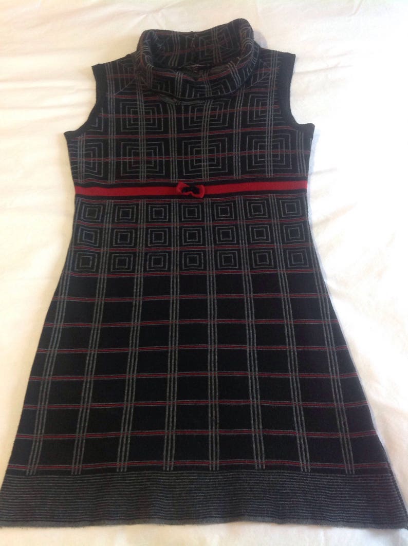 May include: Sleeveless black dress with a red ribbon and bow detail at the waist. The dress features a geometric pattern in black, red, and gray, and a turtleneck collar.