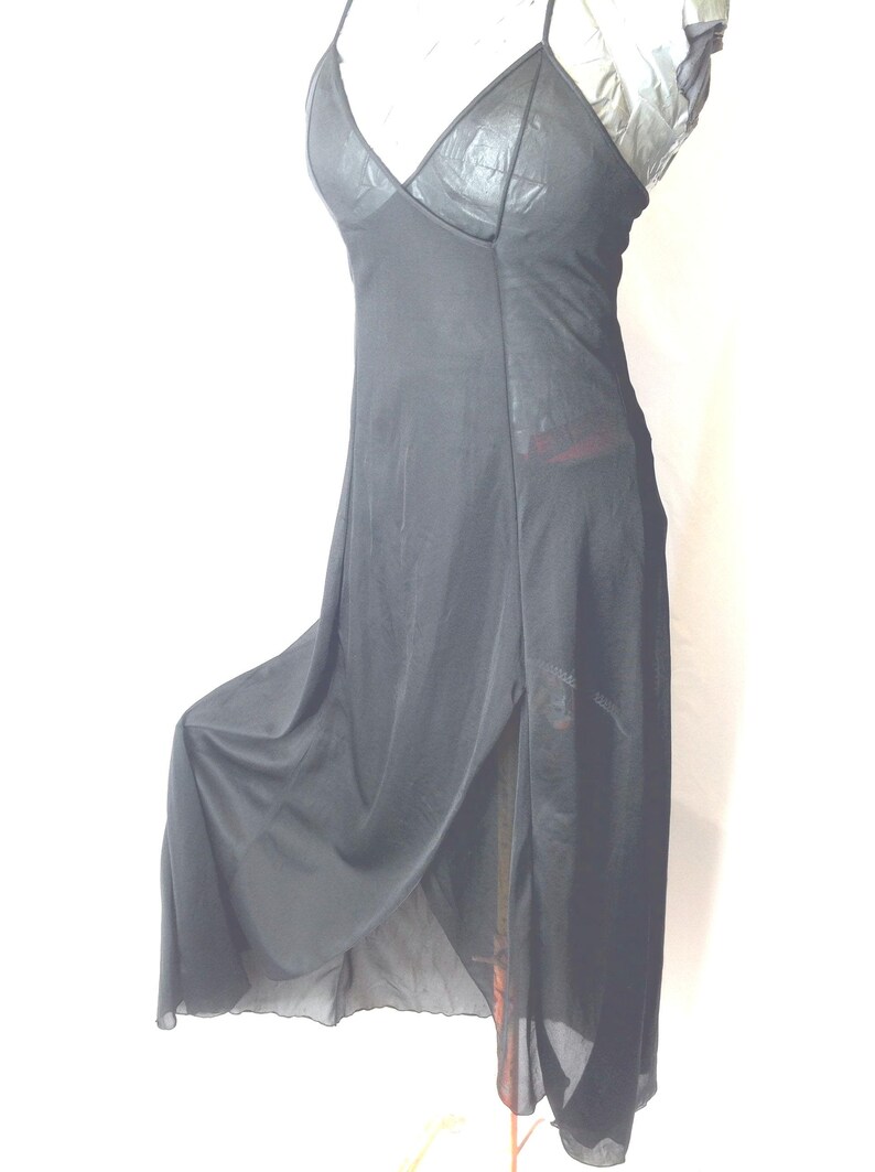 May include: Black slip dress with a V-neck and spaghetti straps. The dress features a high slit on the side and a flowing, sheer skirt. The bodice has a textured appearance. A simple, elegant design.