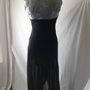 May include: A black maxi dress displayed on a mannequin. The dress features a halter neckline and a fitted bodice that flows into a long, sheer skirt. The fabric appears to be lightweight, creating a flowing silhouette.
