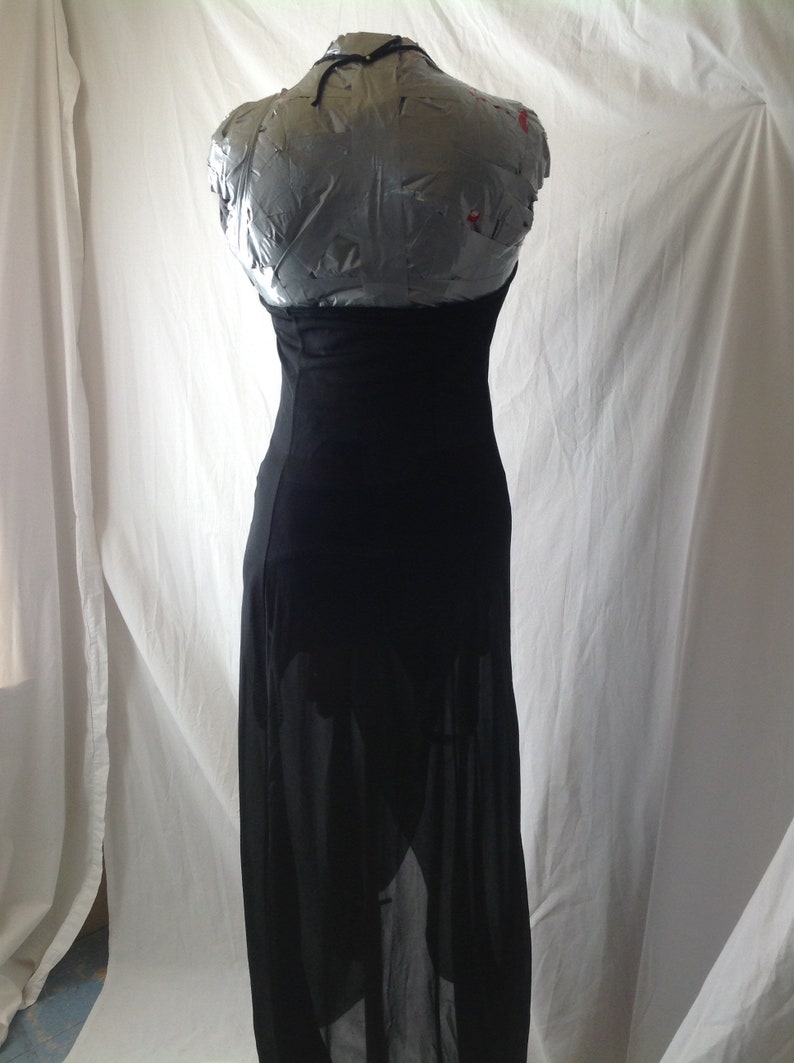 May include: A black maxi dress displayed on a mannequin. The dress features a halter neckline and a fitted bodice that flows into a long, sheer skirt. The fabric appears to be lightweight, creating a flowing silhouette.