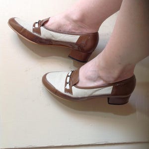 May include: A pair of brown and white heeled shoes with a perforated design and a buckle detail.