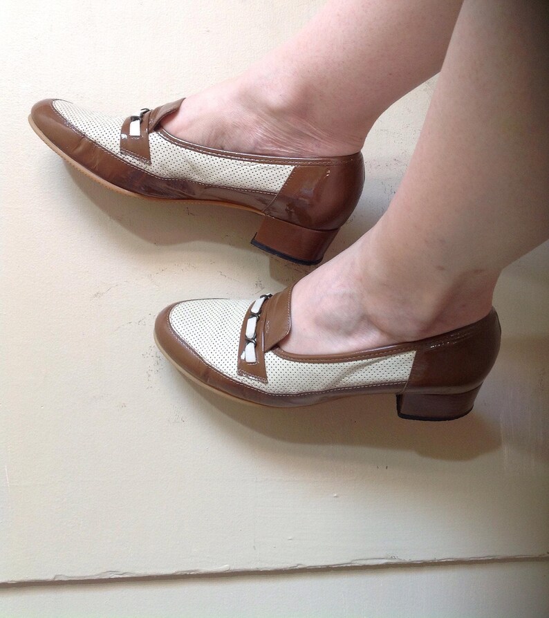 May include: A pair of brown and white heeled shoes with a perforated design and a buckle detail.