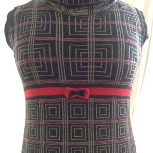 May include: A sleeveless, turtleneck dress with a geometric pattern in black, gray, and red. The dress features a red band at the waist with a small bow detail. The overall design is a retro style.