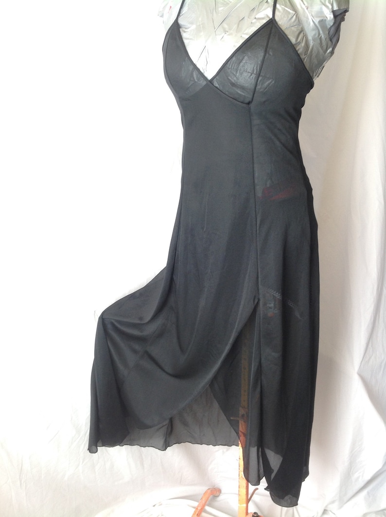 May include: A black slip dress with spaghetti straps and a V-neck. The dress features a high slit on the left side and is made of a sheer, flowing fabric. The dress is displayed on a mannequin.